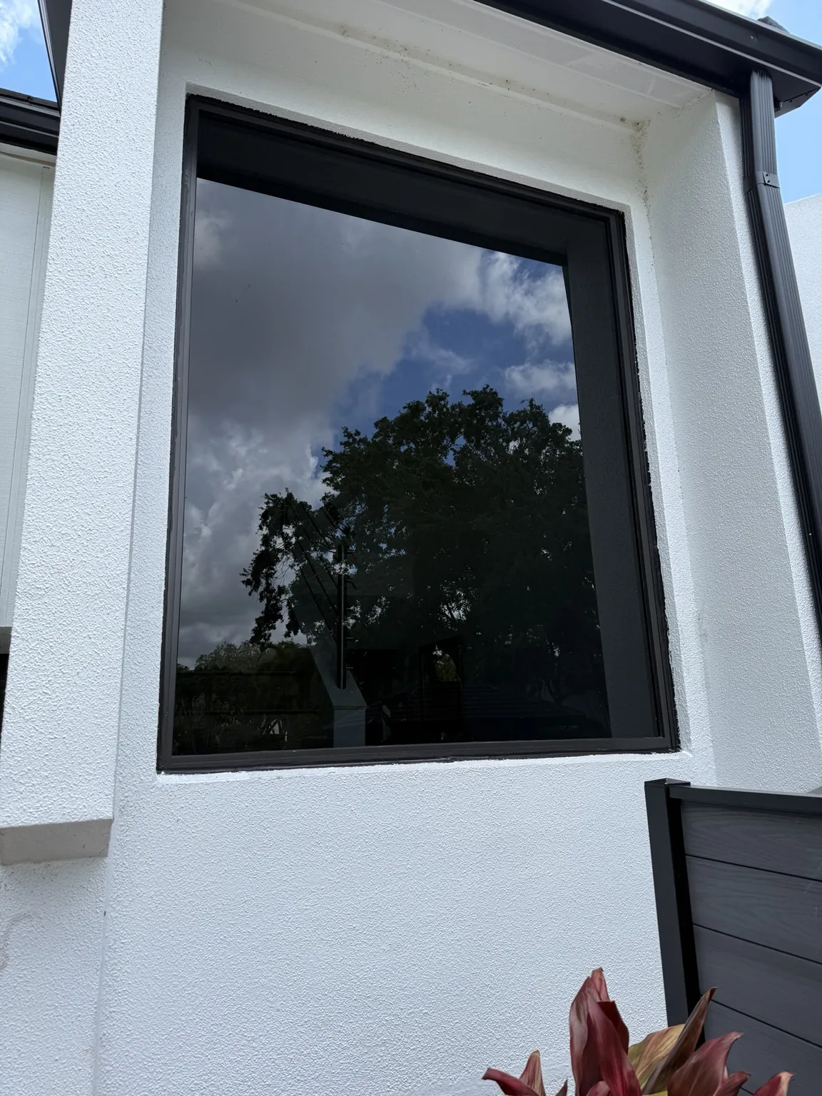 Completed black-framed impact picture window on white stucco home